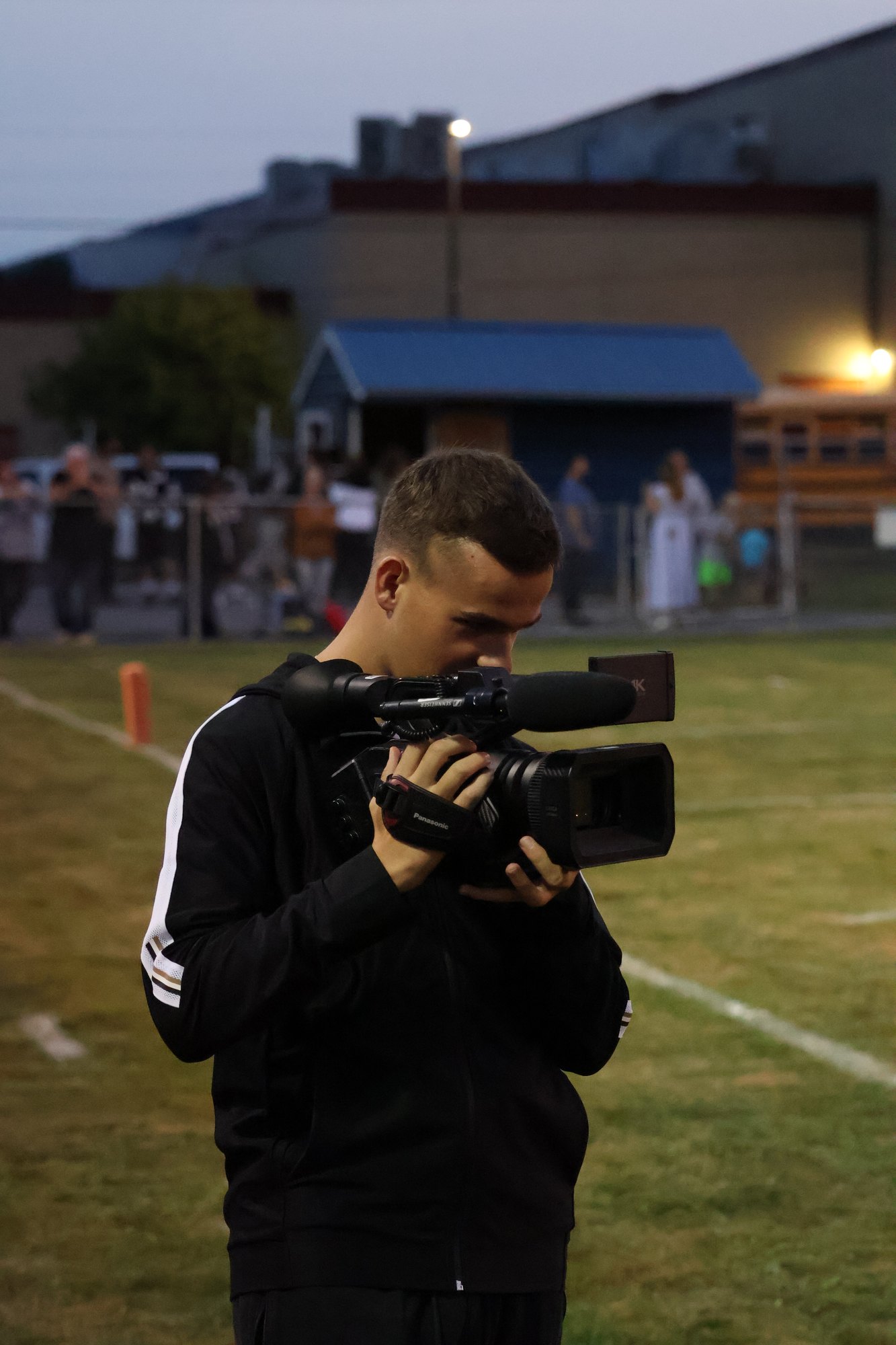 Joseph Draper films a football game from the sideline with a professional Panasonic camera as a multimedia journalist
